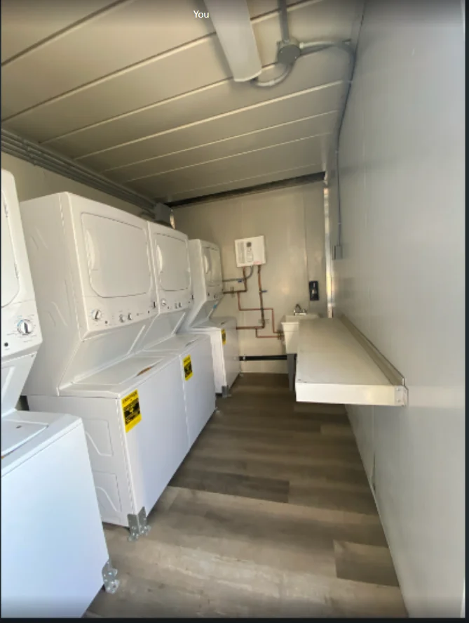 Laundry container interior with stacked washers and dryers beside a work counter