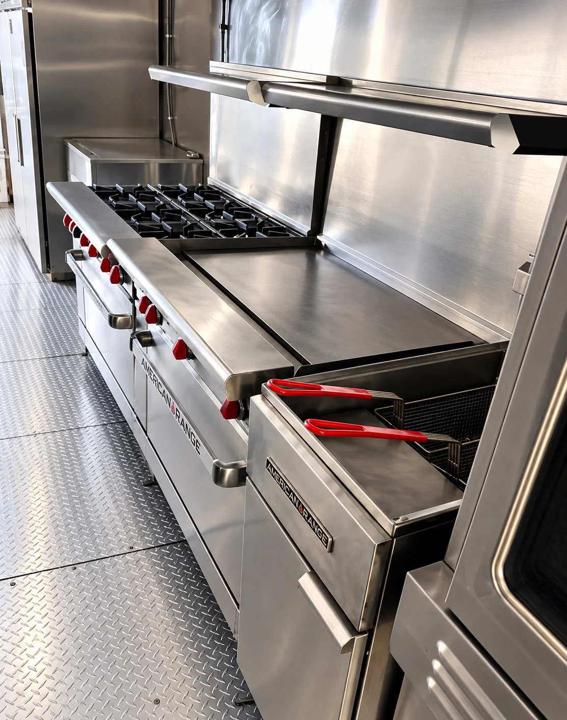 Commercial kitchen trailer cooking line with a range, griddle and fryer beneath an extraction hood