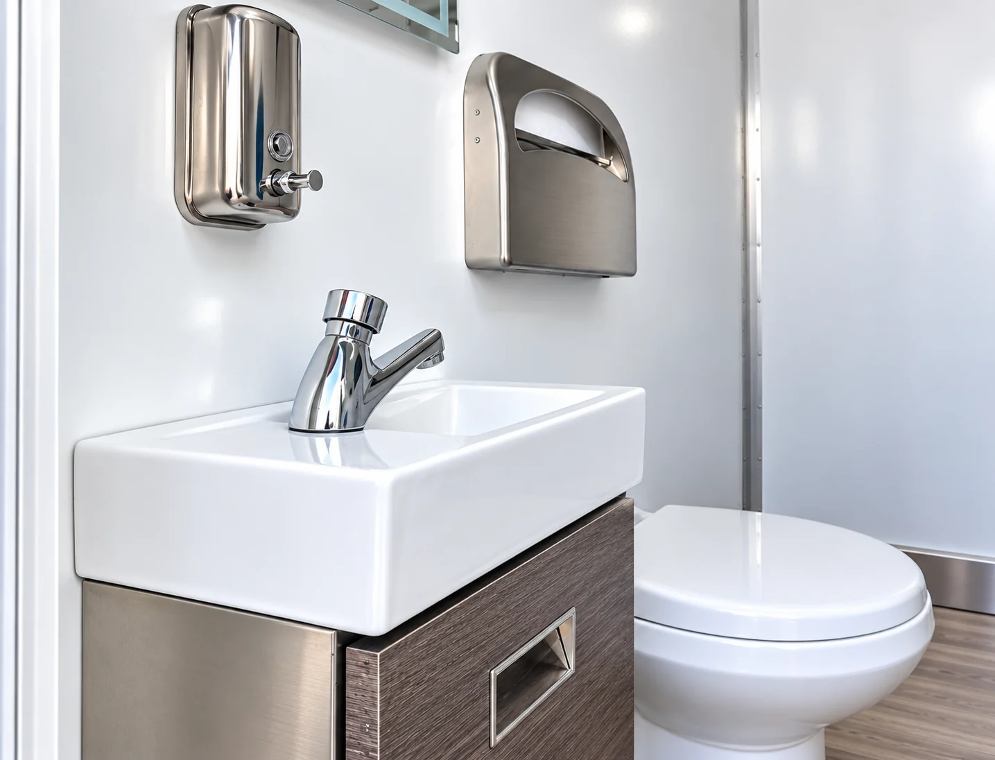Restroom washbasin and toilet with wall-mounted soap and towel dispensers
